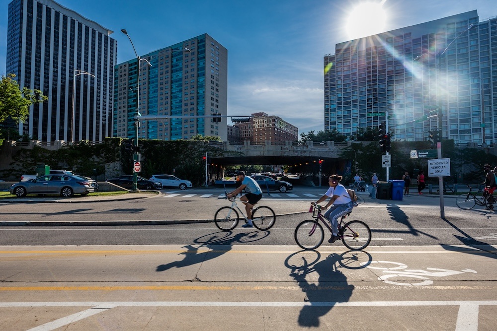 View from Lake Michigan shore showing cyclists and cars with Lake Shore Drive bridge over Belmont Ave in background